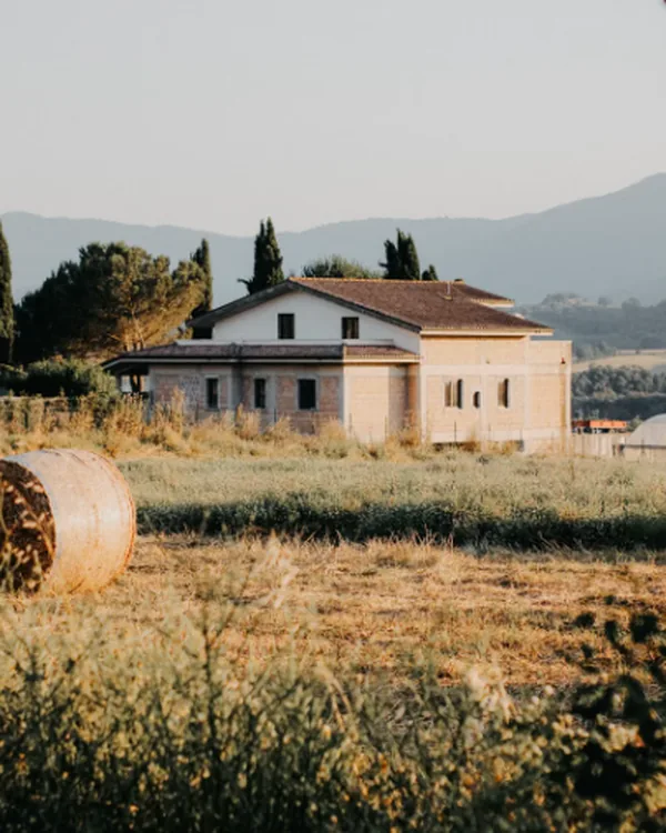 Casale di campagna con un prato e balle di fieno, colline sullo sfondo